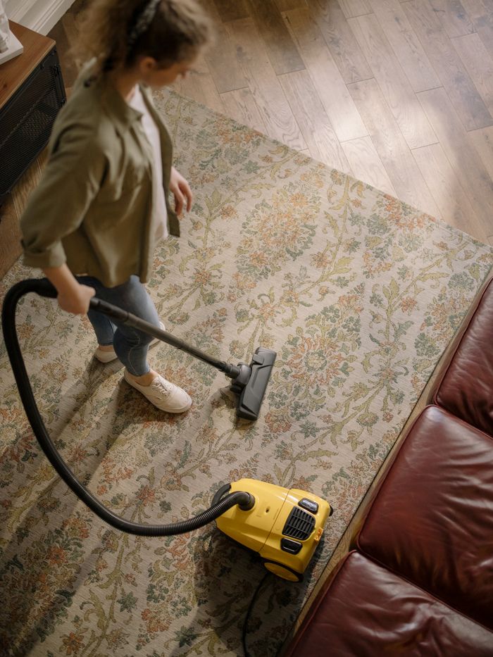 Top-down view of a woman vacuuming a carpet in her home, emphasizing cleanliness and household care.